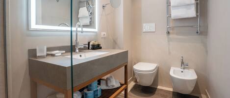 A modern bathroom with a glass-enclosed shower, a vanity with a sink, a bidet, and a towel rack.