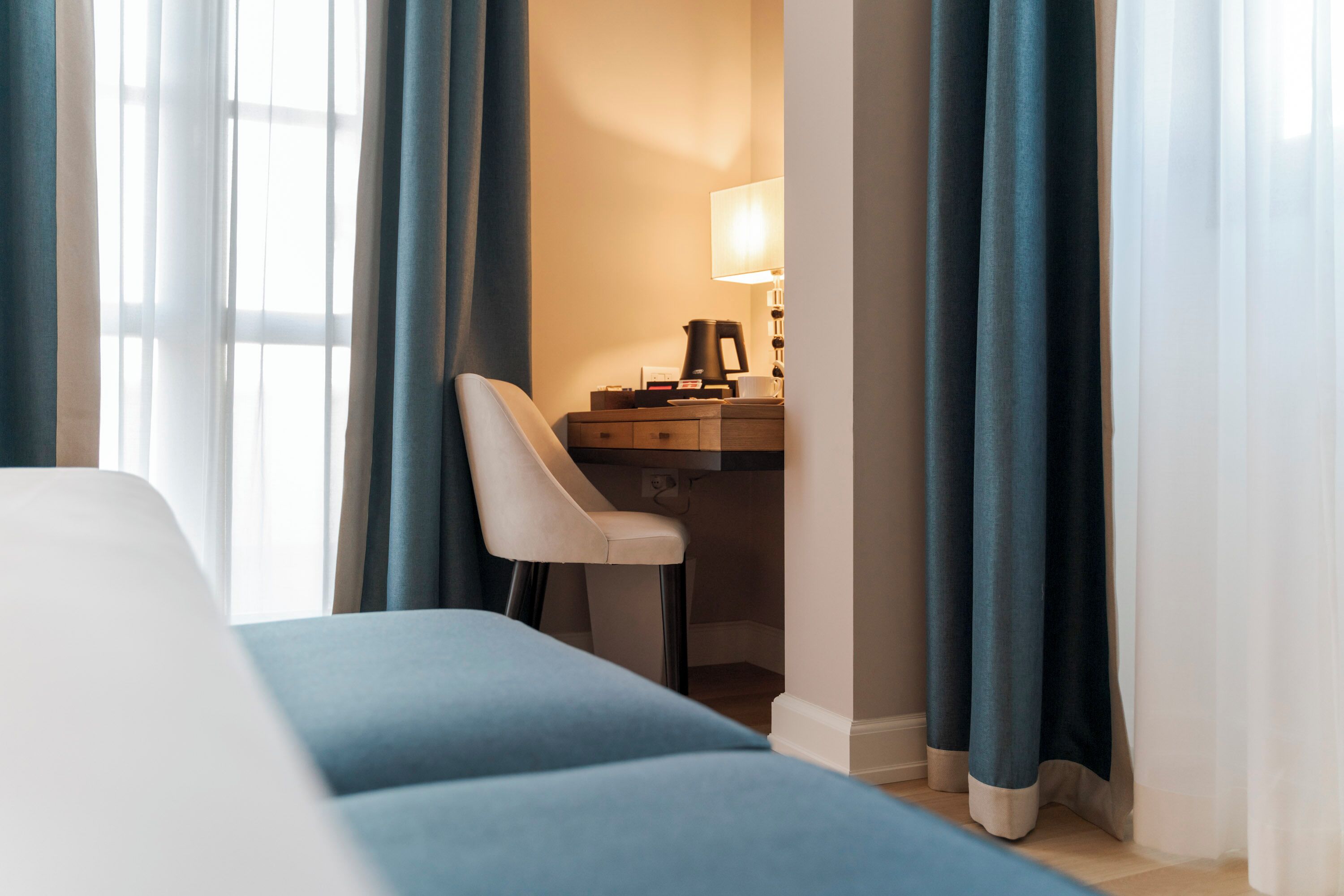 A hotel room with a bed, a desk with a lamp, and curtains.