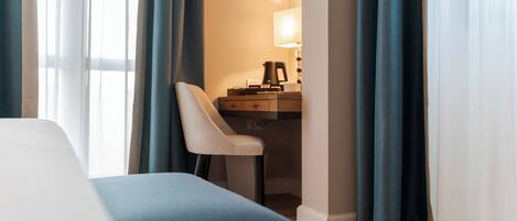 A hotel room with a bed, a desk with a lamp, and curtains.
