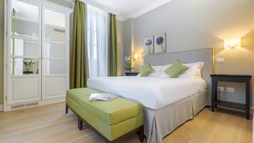 Una habitación de hotel con una cama, un reposapiés verde, una mesita de noche y una lámpara de pared.