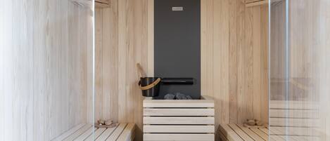 Un sauna avec des bancs en bois et un appareil de chauffage noir au centre.