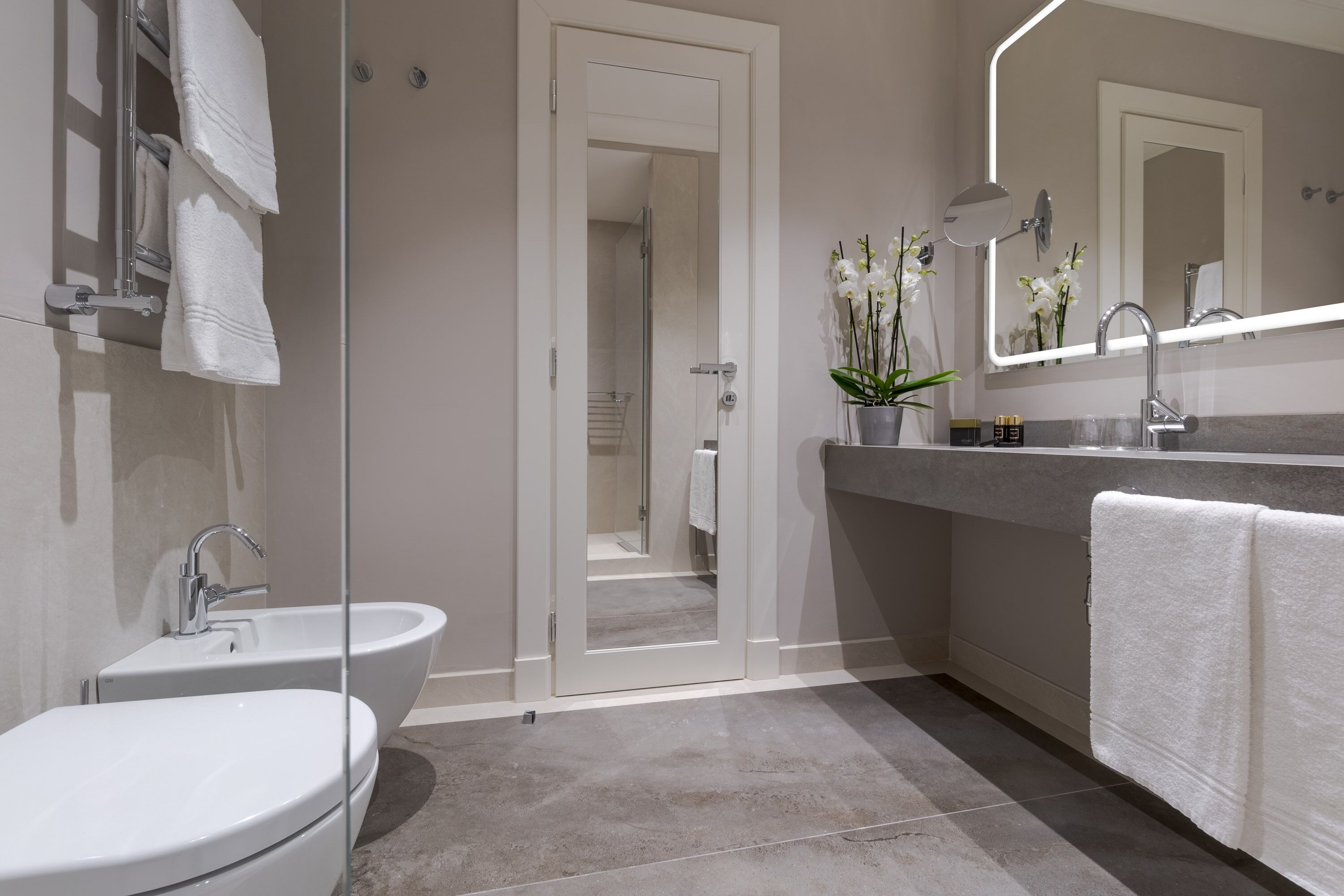A modern bathroom with a glass shower enclosure, a freestanding bathtub, a vanity with a mirror, and a potted orchid.