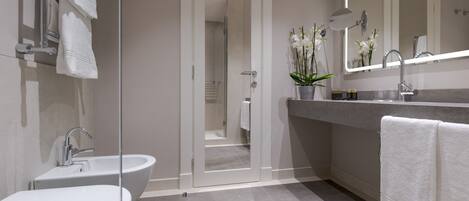 A modern bathroom with a glass shower enclosure, a freestanding bathtub, a vanity with a mirror, and a potted orchid.