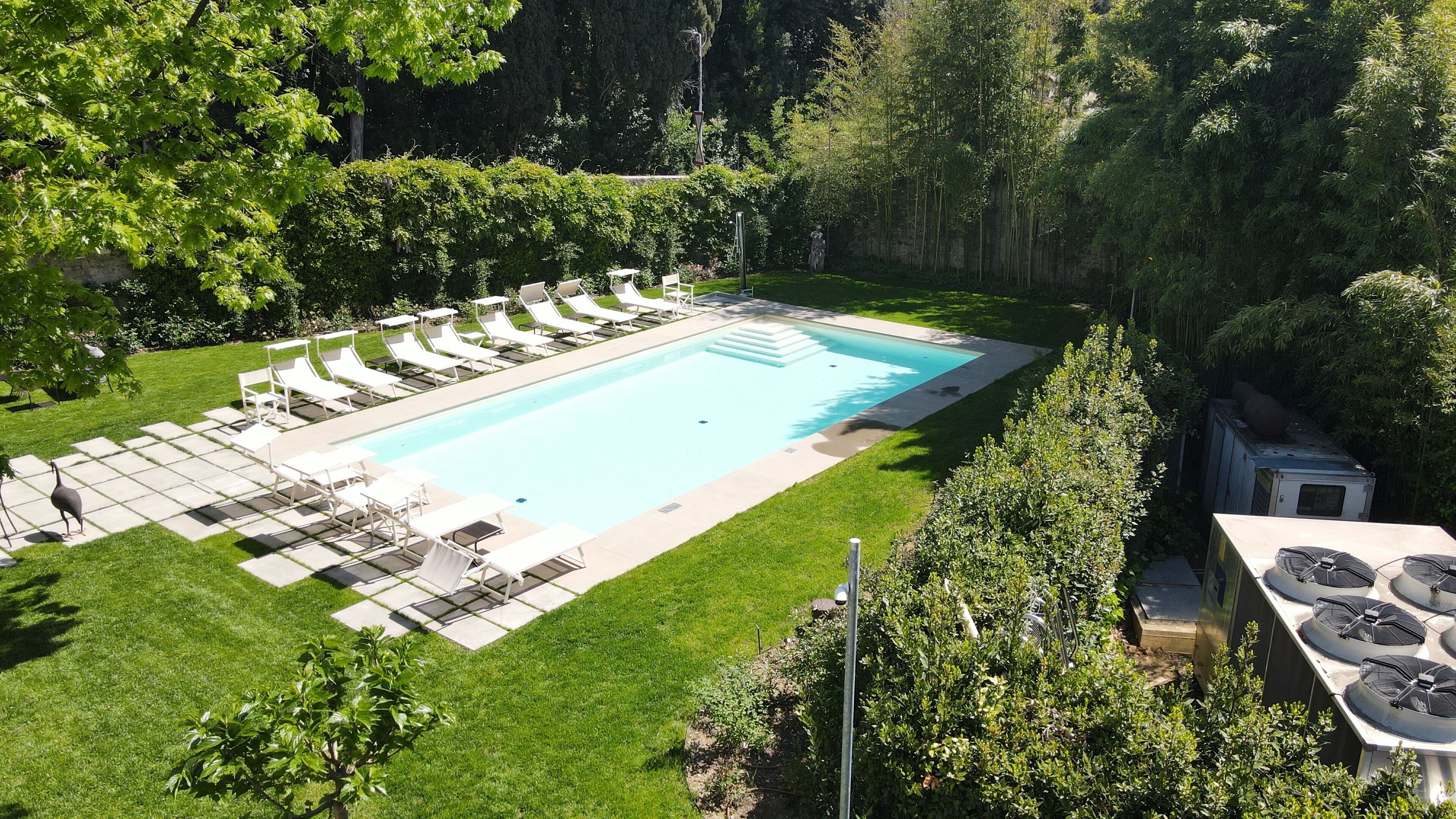 Ein rechteckiger Pool mit Fliesen umgeben, mit einem gepflegten Rasen und Bäumen.