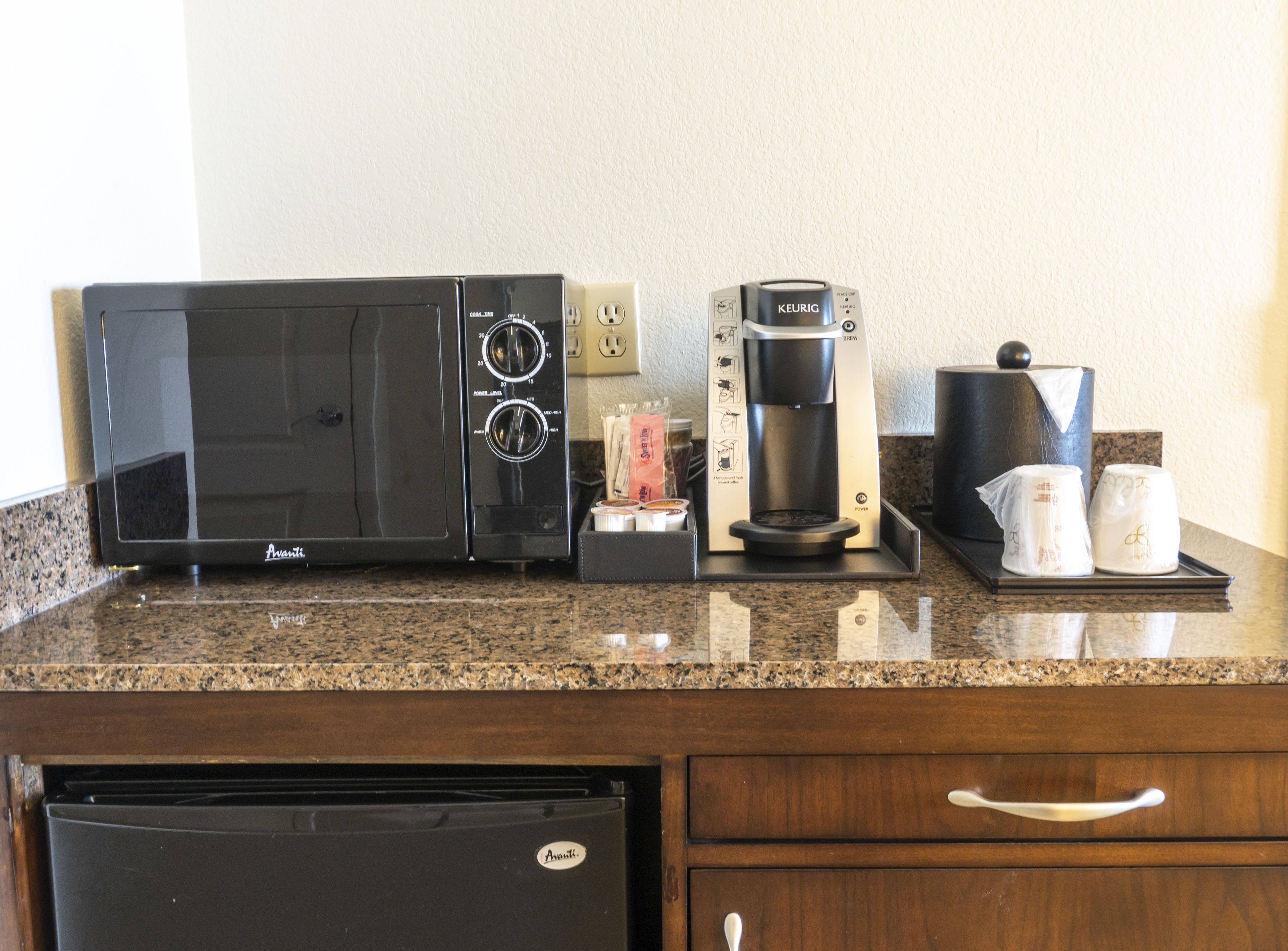 Una kitchenette con microondas, cafetera y jarra para café sobre una encimera de granito.