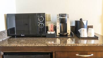 Una kitchenette con microondas, cafetera y jarra para café sobre una encimera de granito.