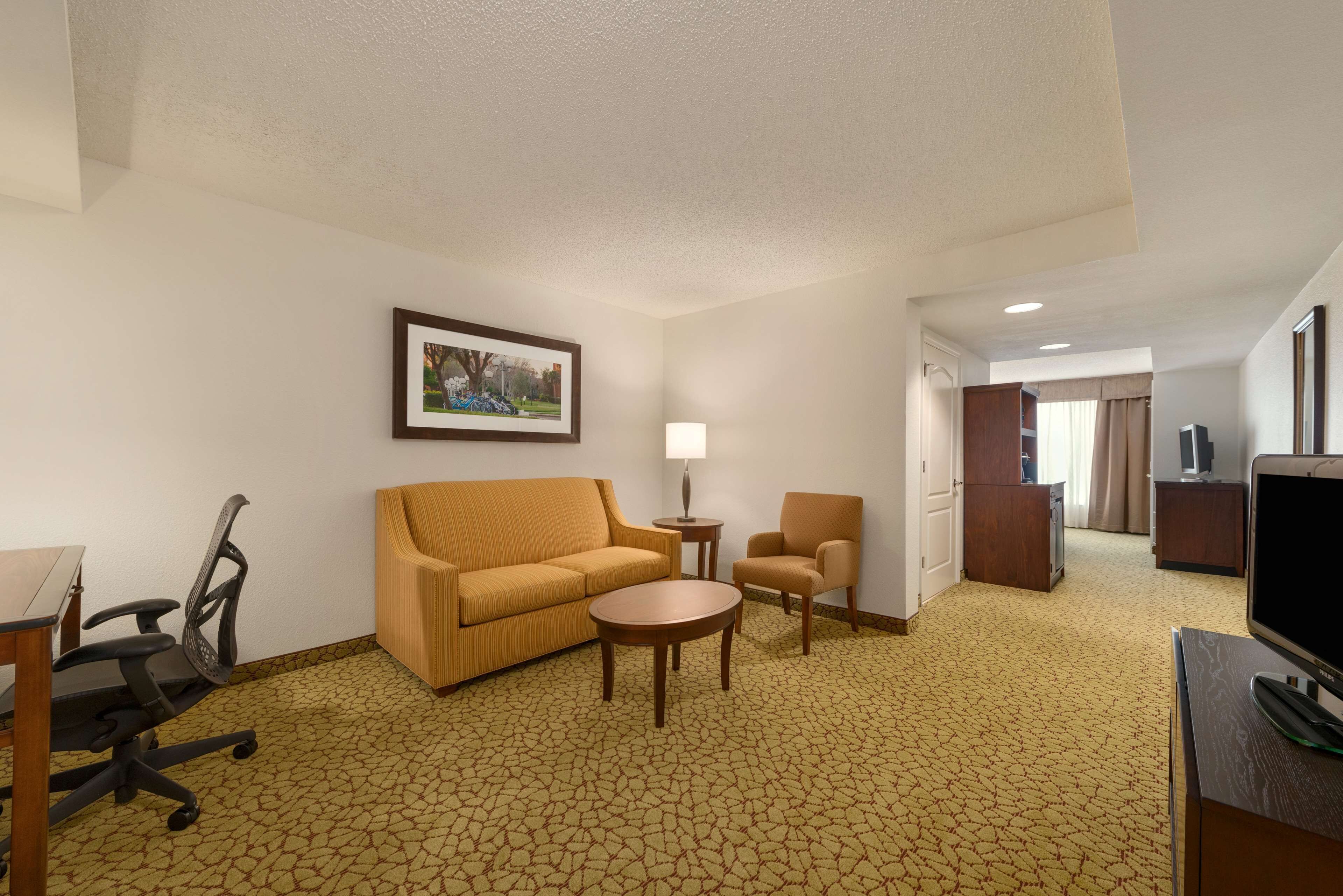 A hotel room with a sofa, armchair, small round table, and a TV.