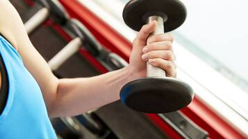 A person holding a dumbbell in a gym with red equipment in the background.