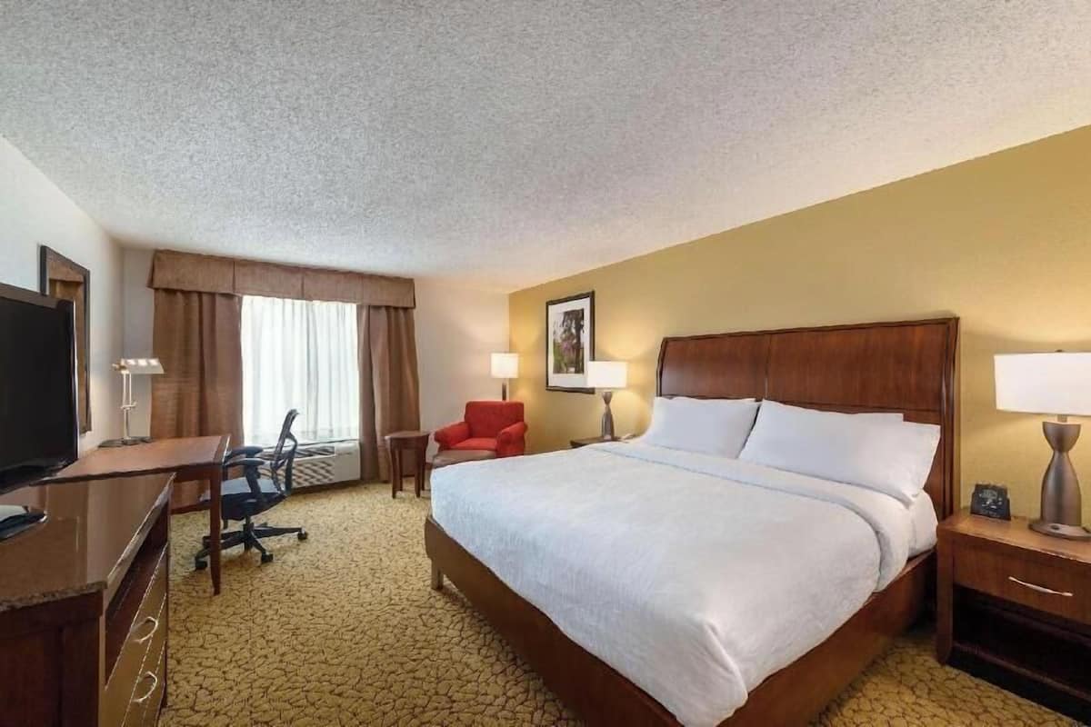 Een hotelkamer met een groot bed, een bureau met stoel, een televisie en een rode fauteuil.