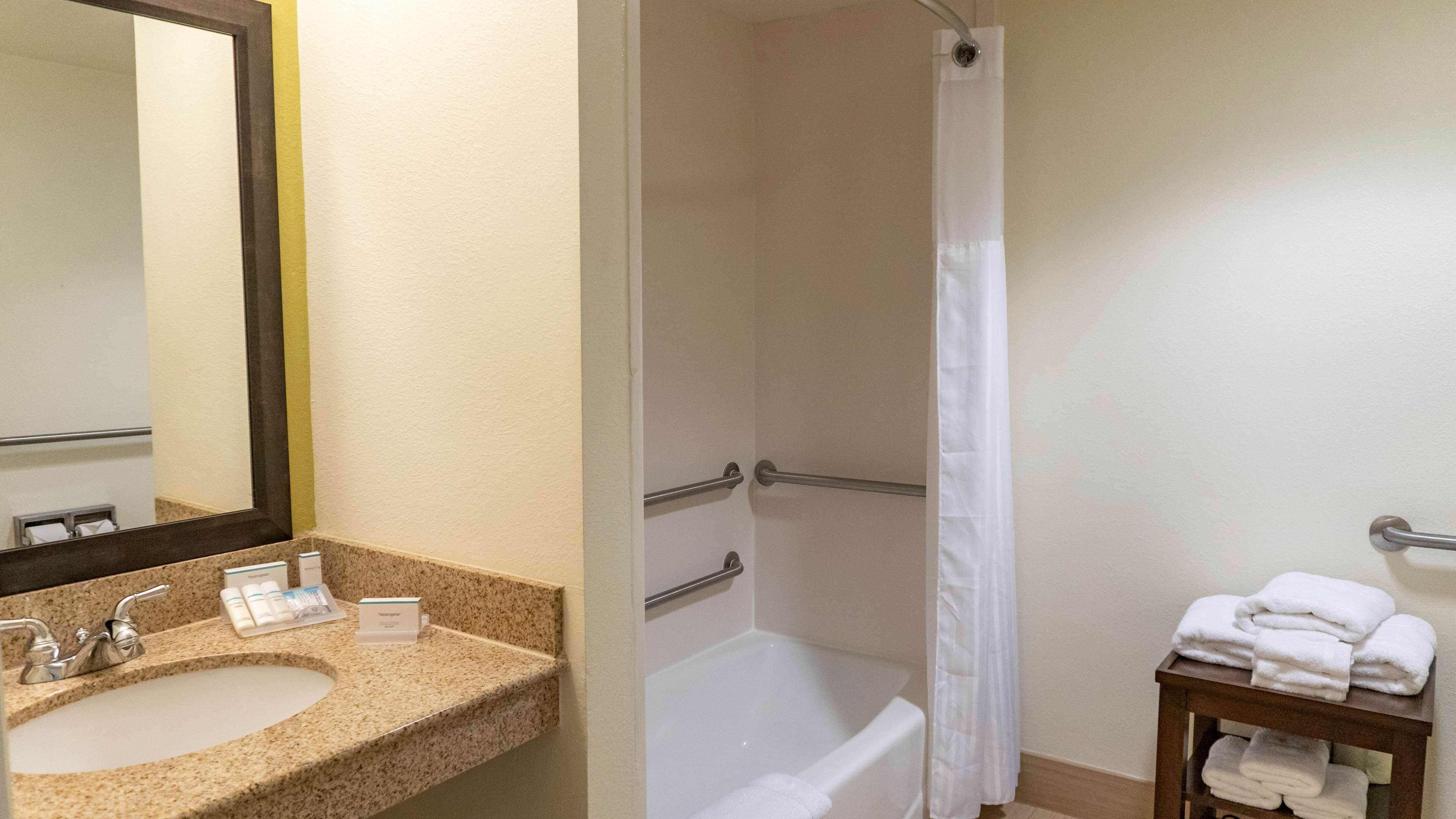 A bathroom with a sink, mirror, shower, and a small table with towels.