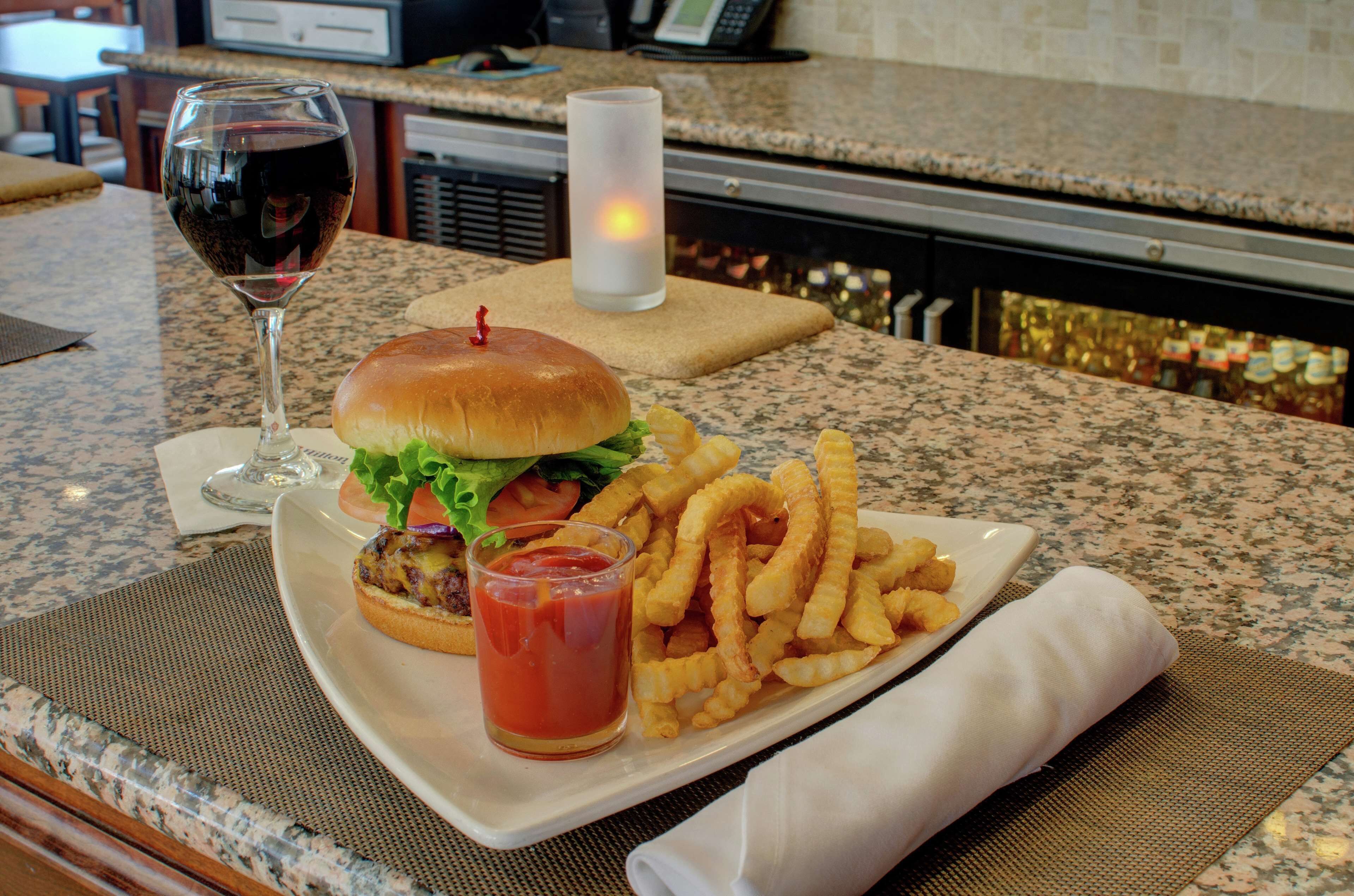 A dining table with a burger, fries, a glass of red wine, and a candle.