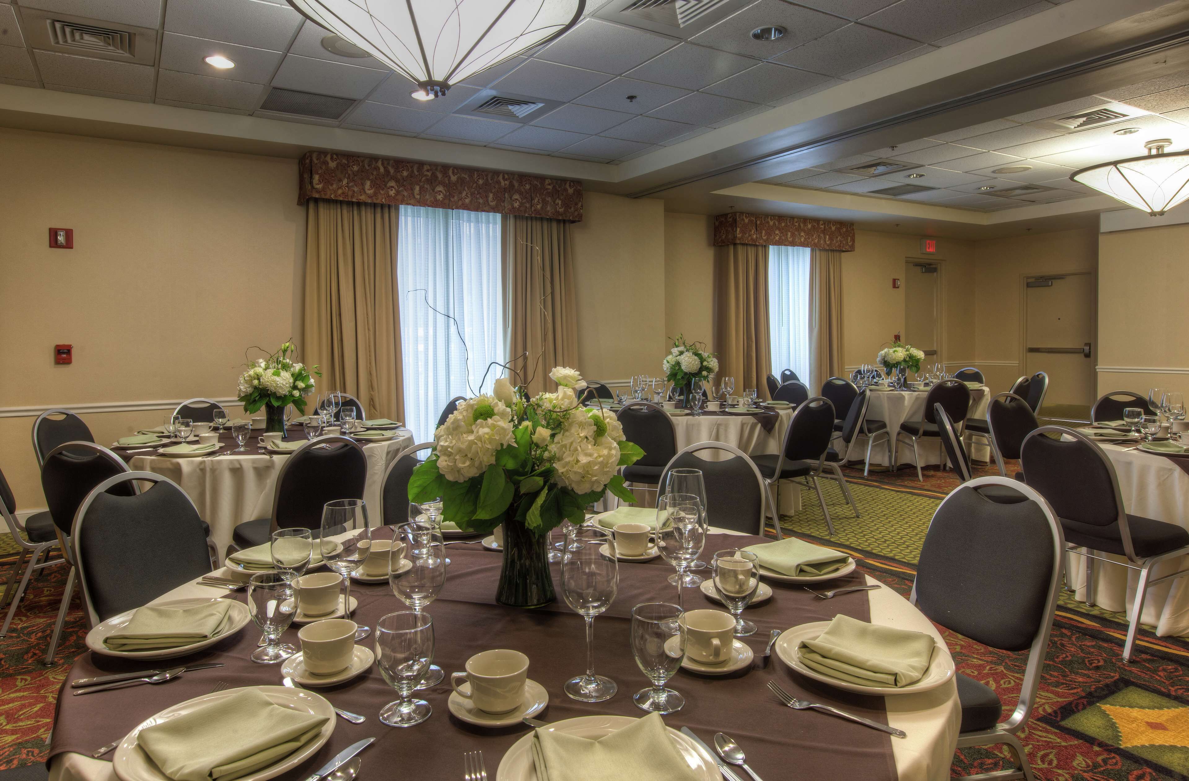 A banquet hall with round tables set for dining, each with white tablecloths, chairs, and floral centerpieces.