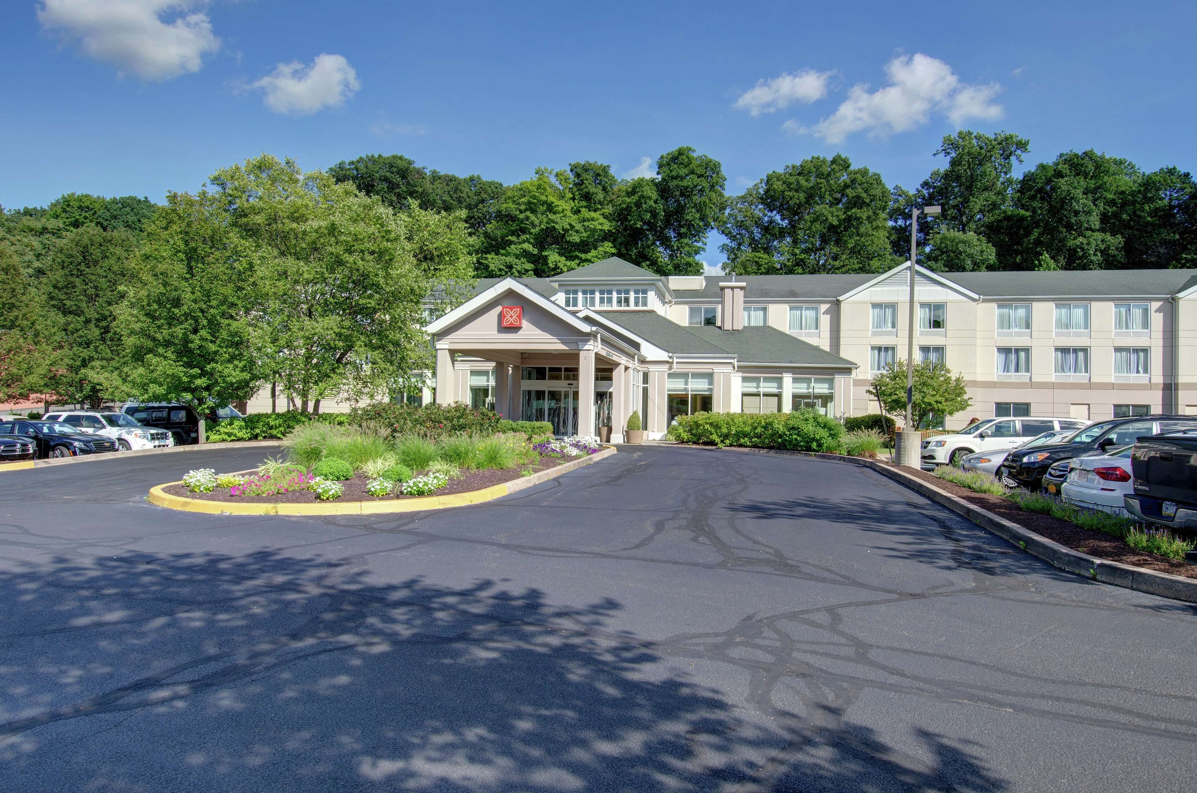 A hotel with a central entrance, parking lot, and surrounding greenery.