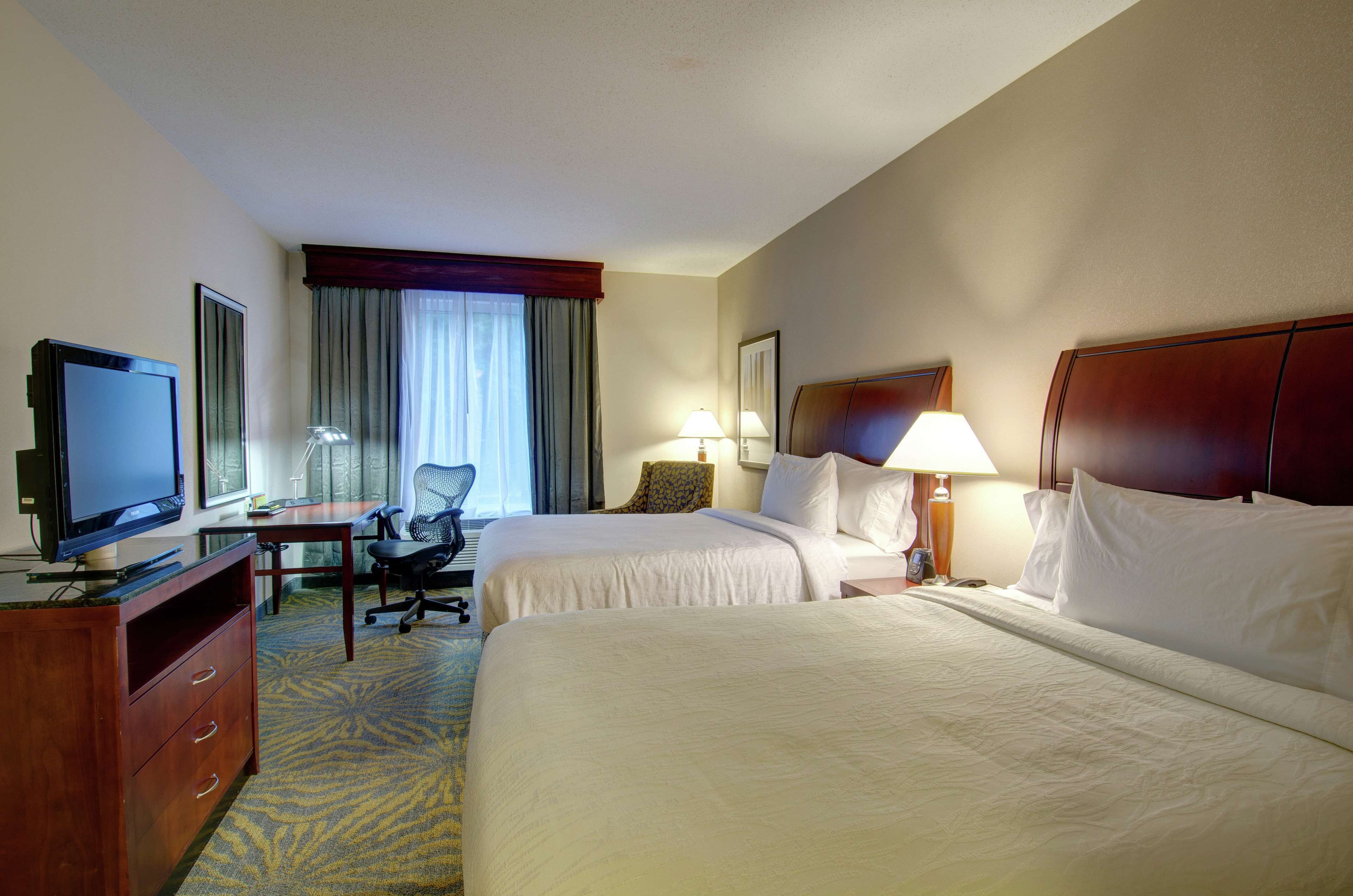 A hotel room with two beds, a desk with a computer, a television, and a chair.