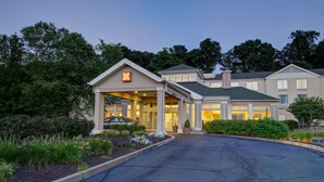 A hotel entrance with a covered driveway, landscaped gardens, and a car parked in front. - Hilton Garden Inn Norwalk (Norwalk)