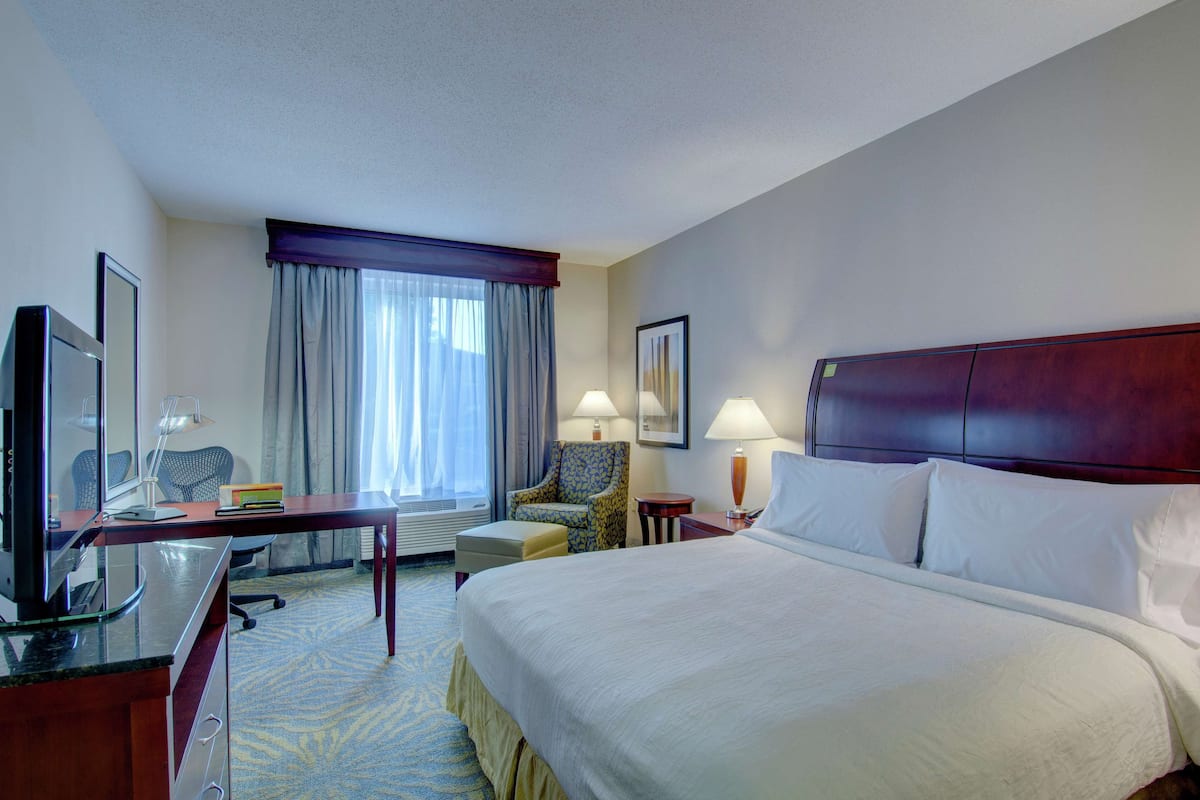 A hotel room with a large bed, a desk with a computer, a chair, a lamp, and a television.