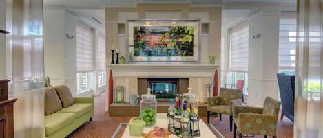 Amplia sala de estar con chimenea, un sofá verde, una mesa de centro con objetos decorativos y una gran pantalla de televisión.