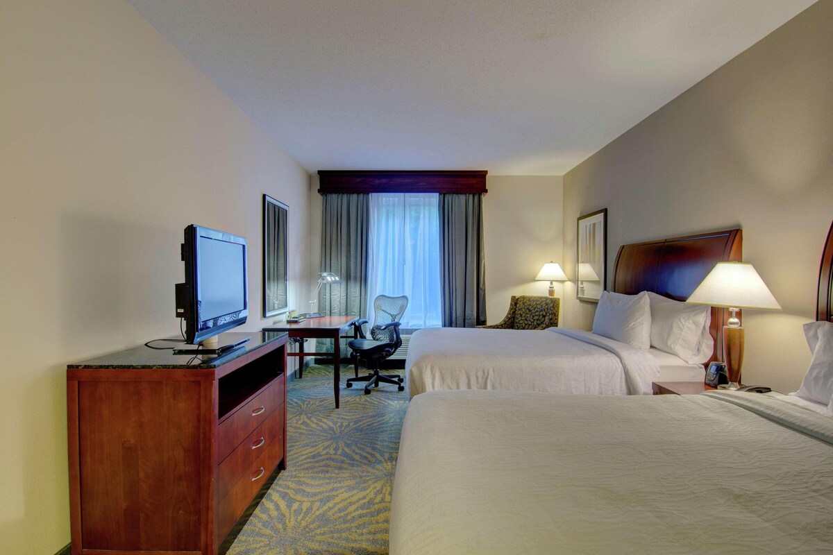 A hotel room with two beds, a desk with a computer, a TV, and a chair.