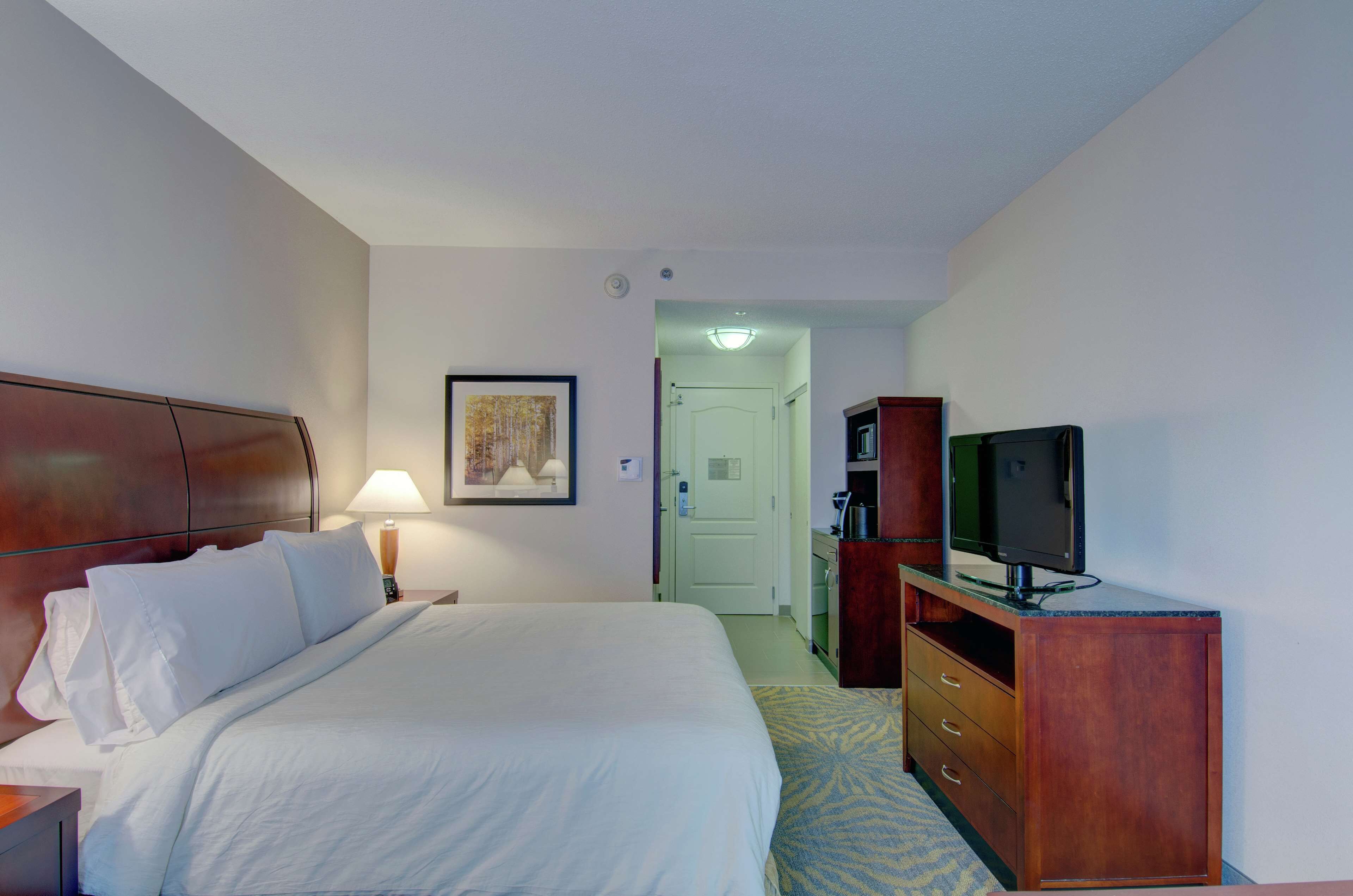 Une chambre d’hôtel avec un grand lit, une commode en bois, une télévision et une porte donnant sur une salle de bain.