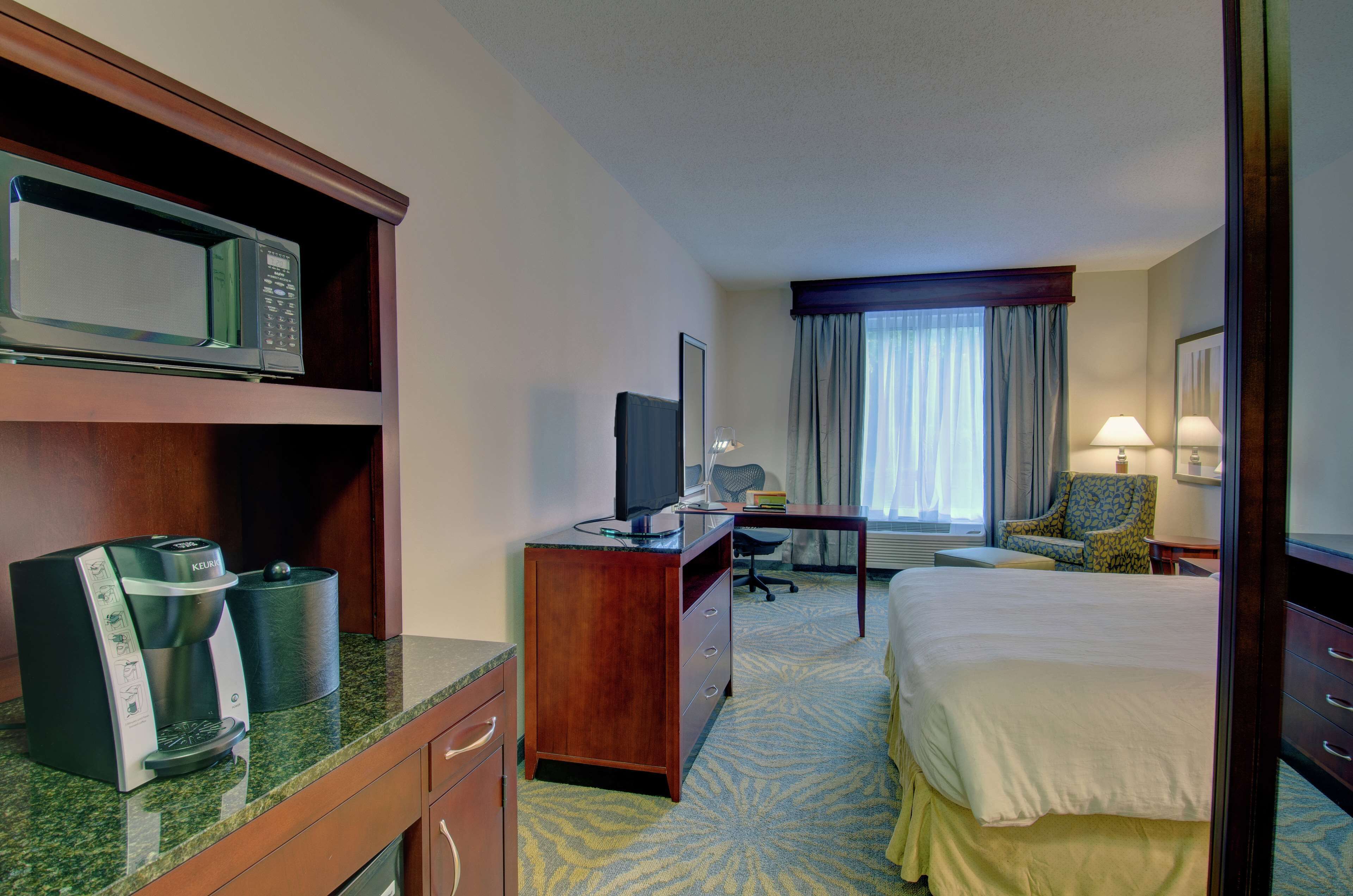 A hotel room with a bed, a desk with a computer, a coffee maker, and a television.