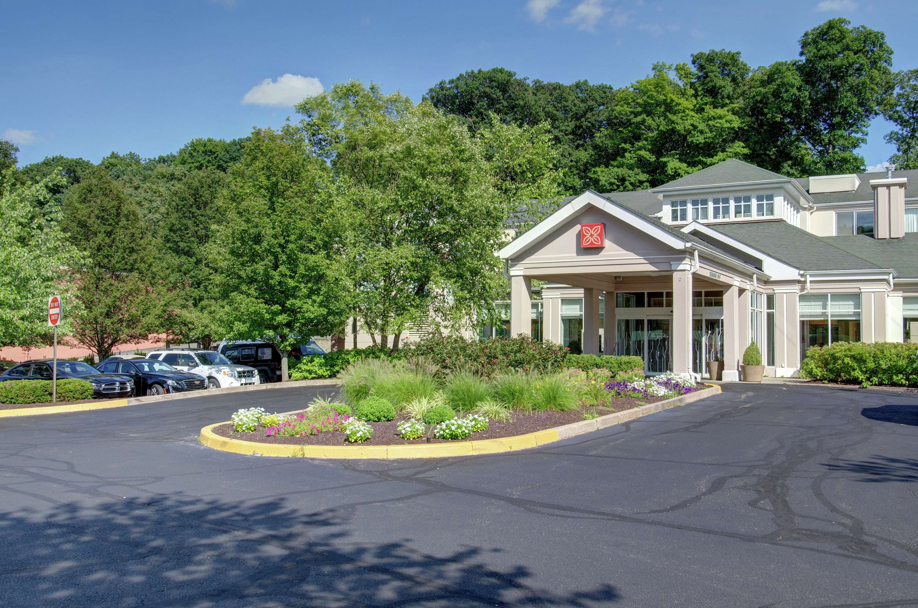 A hotel entrance with a covered driveway, parking lot, and surrounding greenery.