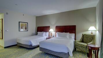 A hotel room with two beds, a chair, a small table, and a lamp.