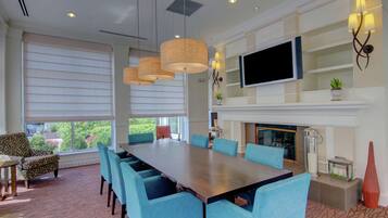 A spacious dining area with a long table and blue chairs, a fireplace, and a flat-screen TV mounted on the wall.