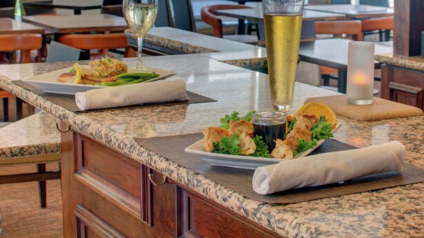 A restaurant interior with a marble countertop, a tall glass of beer, and plates of food. - Hilton Garden Inn Norwalk (Norwalk)