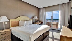 Una habitación de hotel con una cama grande, dos lámparas de noche, un escritorio con una silla, un televisor y un balcón con vista a la ciudad.
