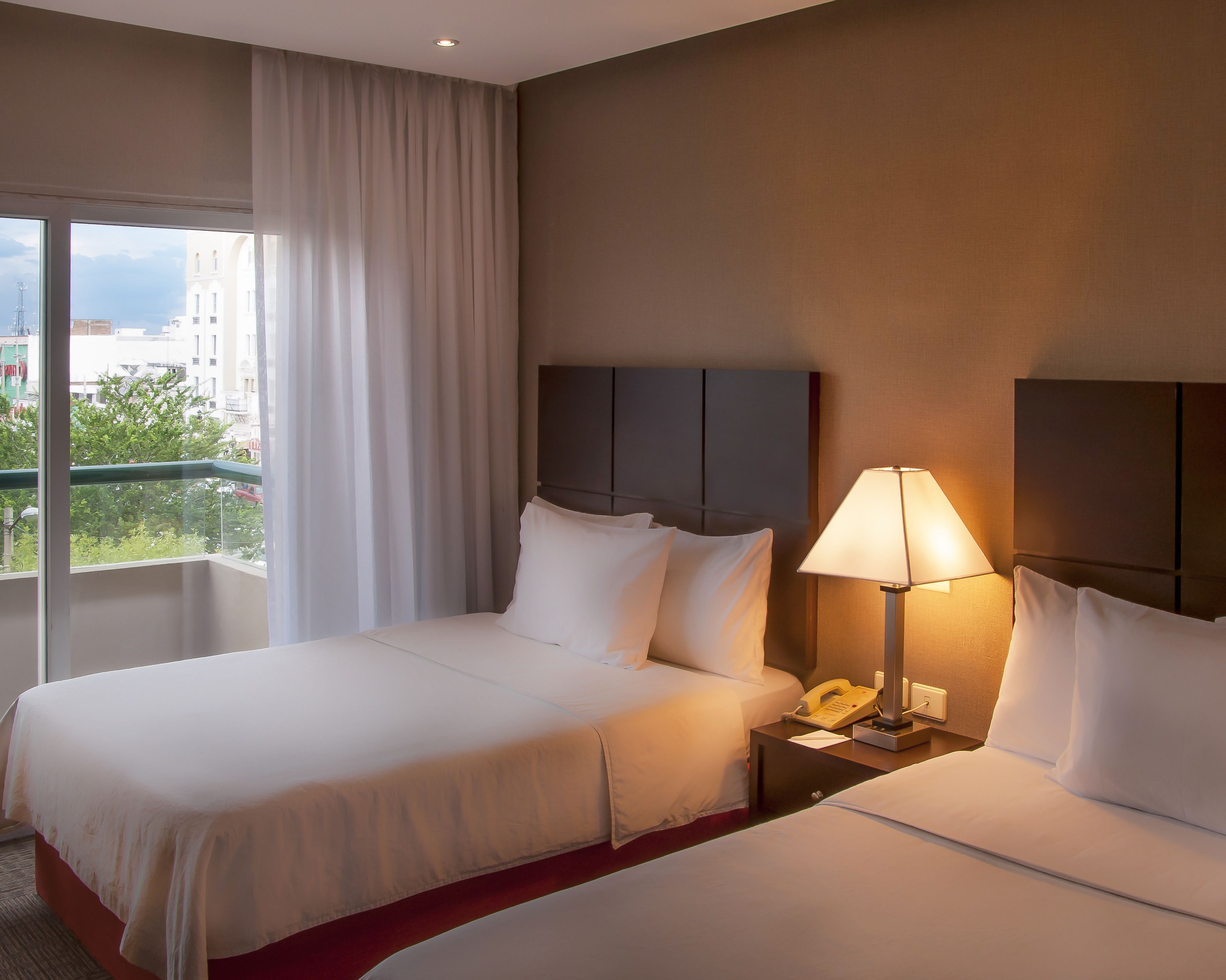 A hotel room with a large bed, a bedside table with a lamp, and a window with curtains.