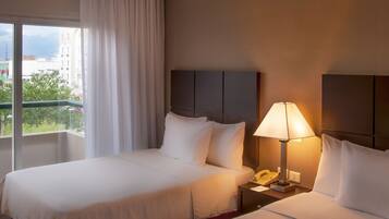 A hotel room with a large bed, a bedside table with a lamp, and a window with curtains.