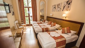 Ein Hotelzimmer mit vier Betten, einem Esstisch, Stühlen, einem Spiegel und Kunstwerken an den Wänden.