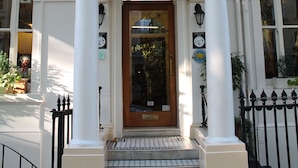 Ein Gebäude mit einem Schild, auf dem „Shakespeare“ über dem Eingang steht, mit einer Holztür, weißen Säulen und einem schwarzen schmiedeeisernen Balkon.