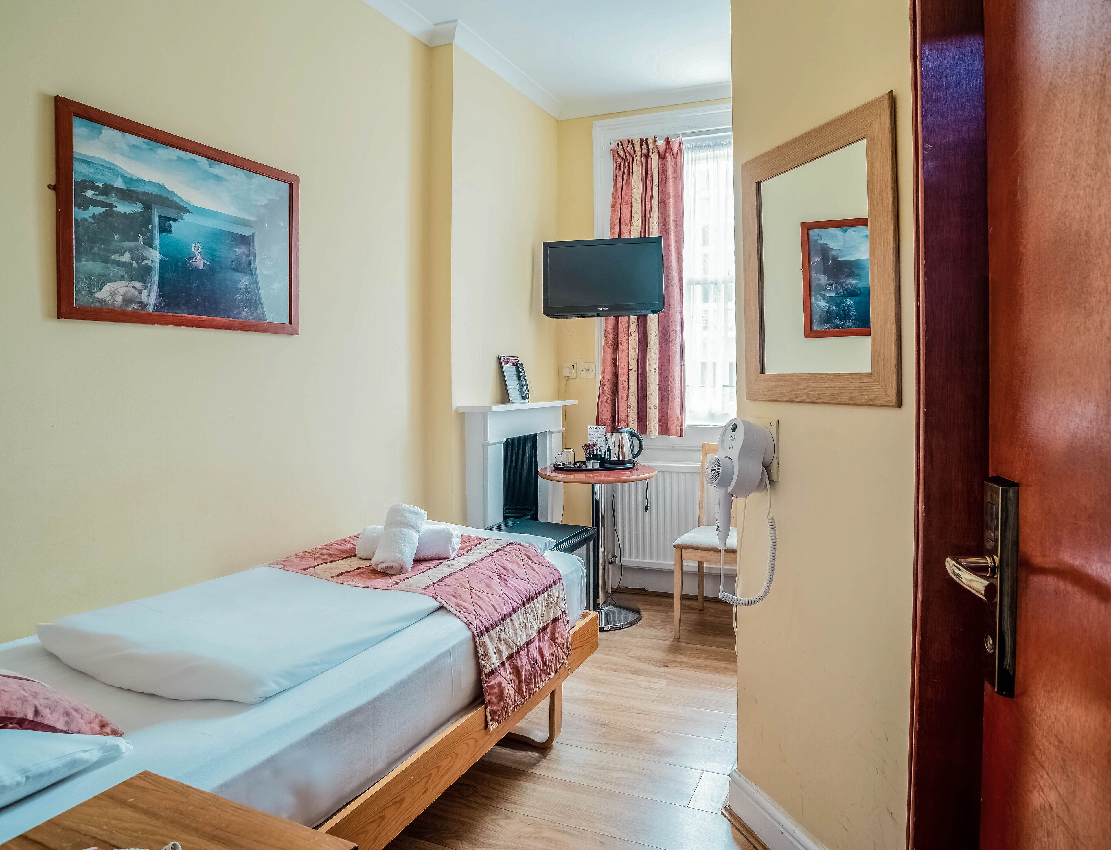 Una camera d'albergo con un letto, una scrivania con un computer, una TV e una finestra con tende.