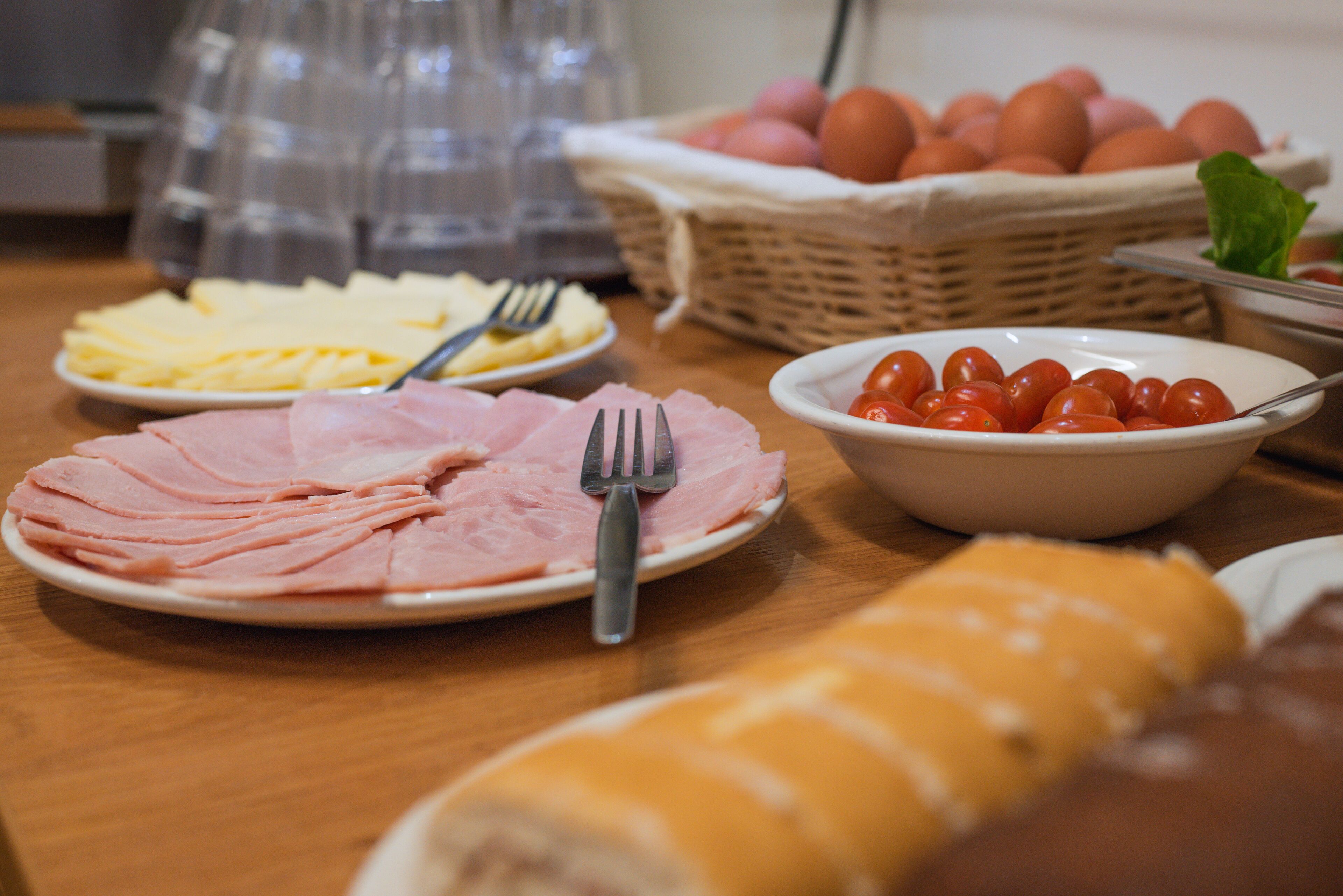 A buffet table with various food items including sliced ham, cheese, and cherry tomatoes.