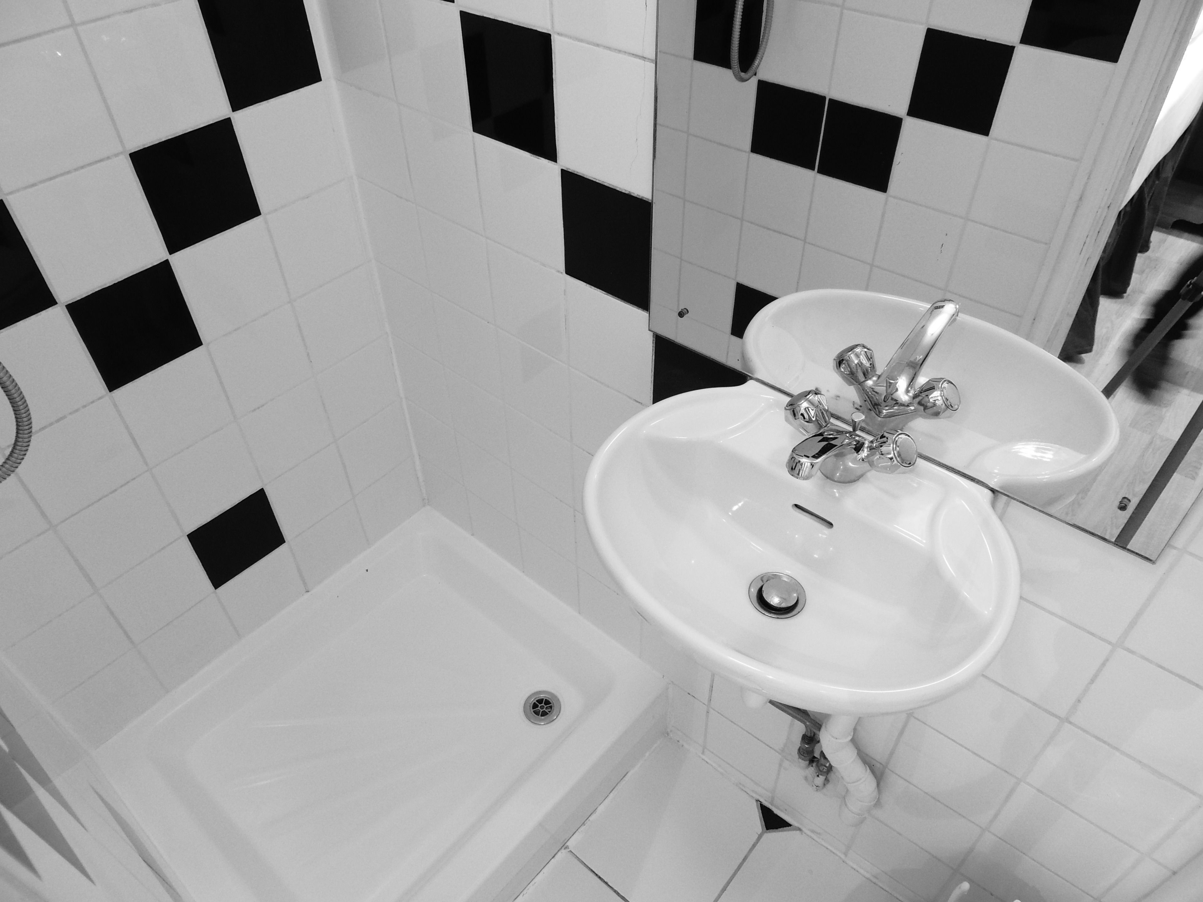 A bathroom with a white sink, a mirror, and black and white checkered tiles on the wall.