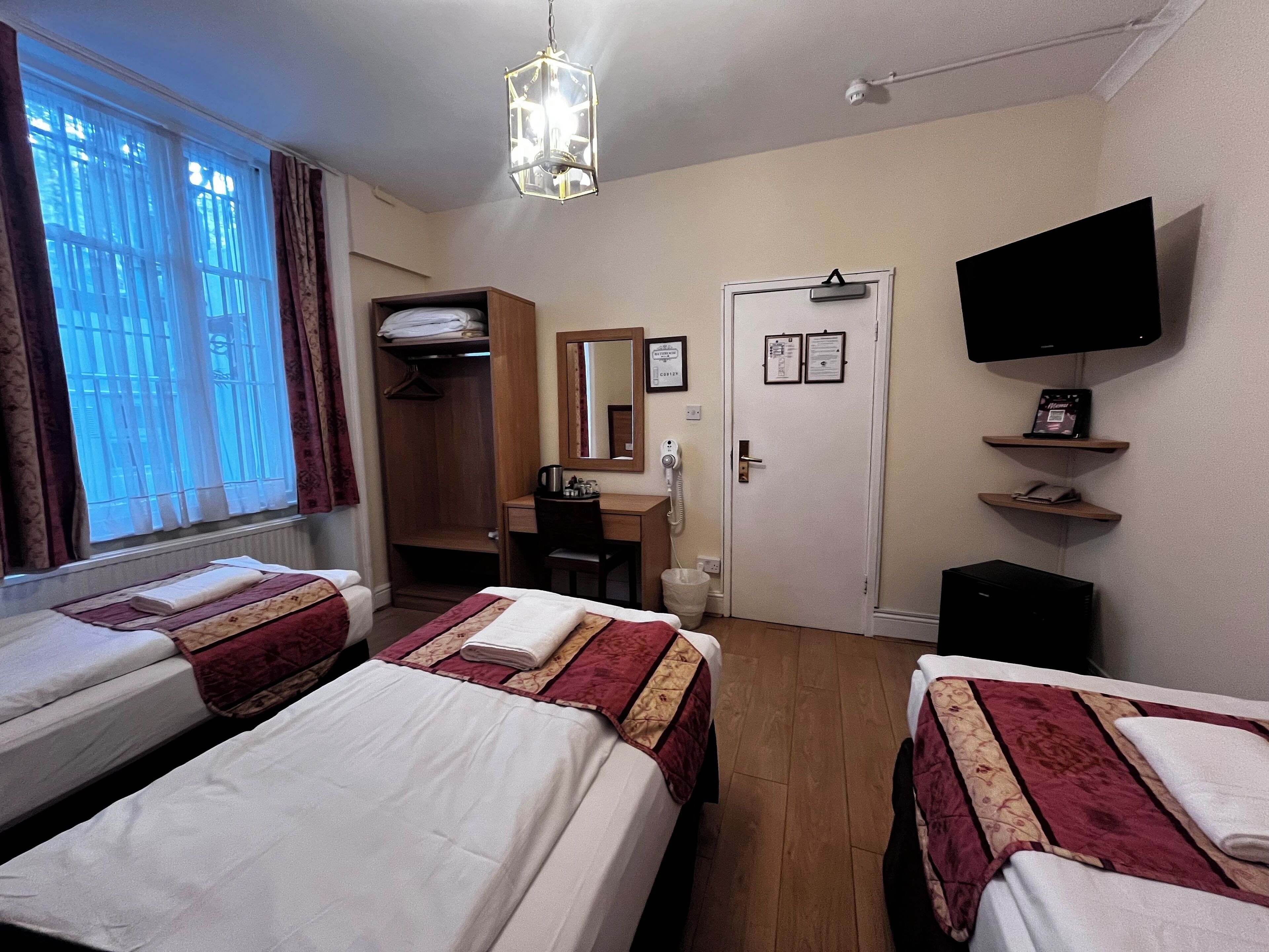 A hotel room with two beds, a desk, a chair, a wardrobe, a television, and a door with a lock.