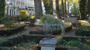 Ein Park mit einer Bank, einem Brunnen und ordentlich geschnittenen Hecken.
