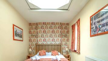 A bedroom with a skylight, patterned wallpaper, a wooden bed frame, and a framed picture on the wall.