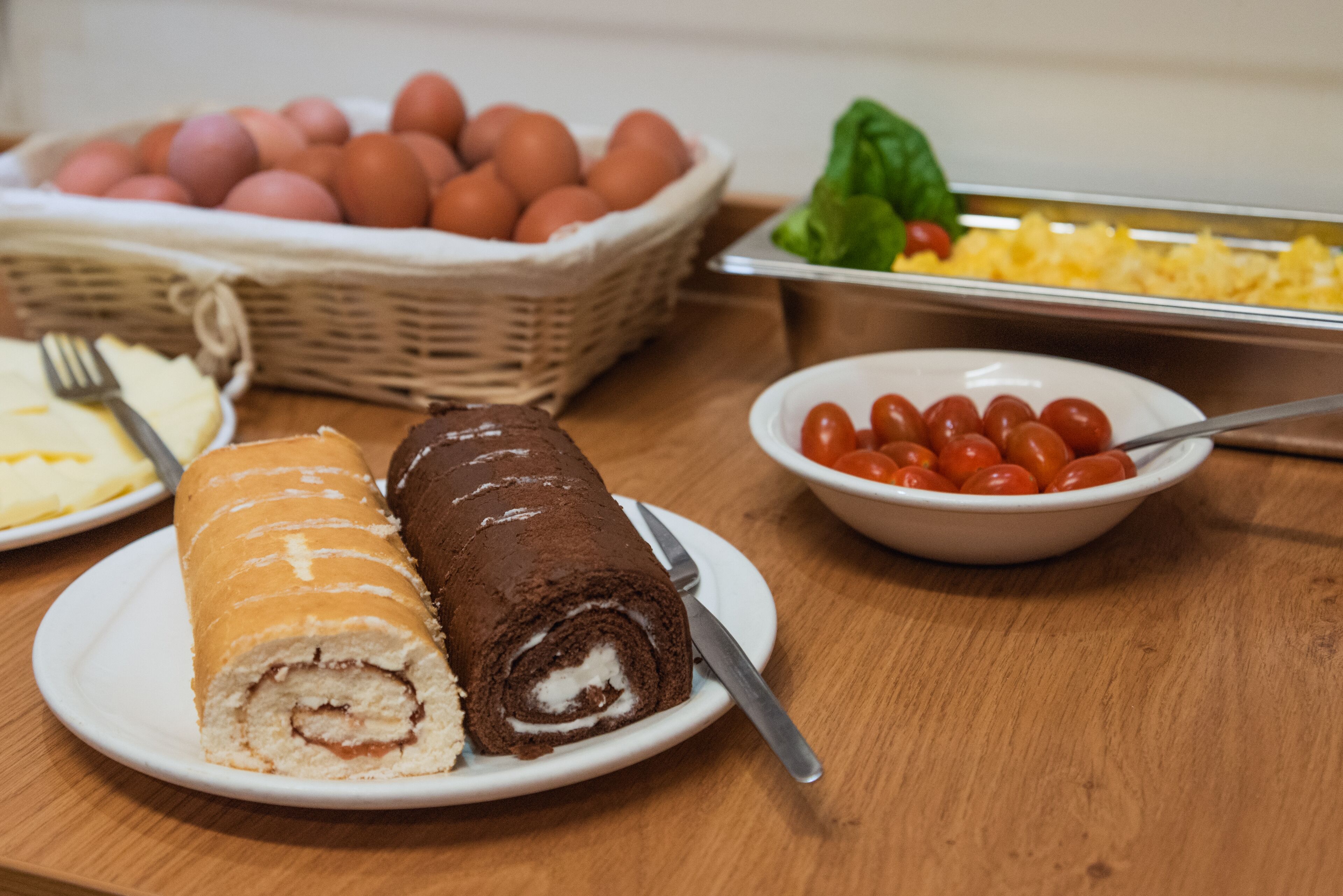 A buffet table with various food items including a chocolate roll, eggs, and cherry tomatoes.