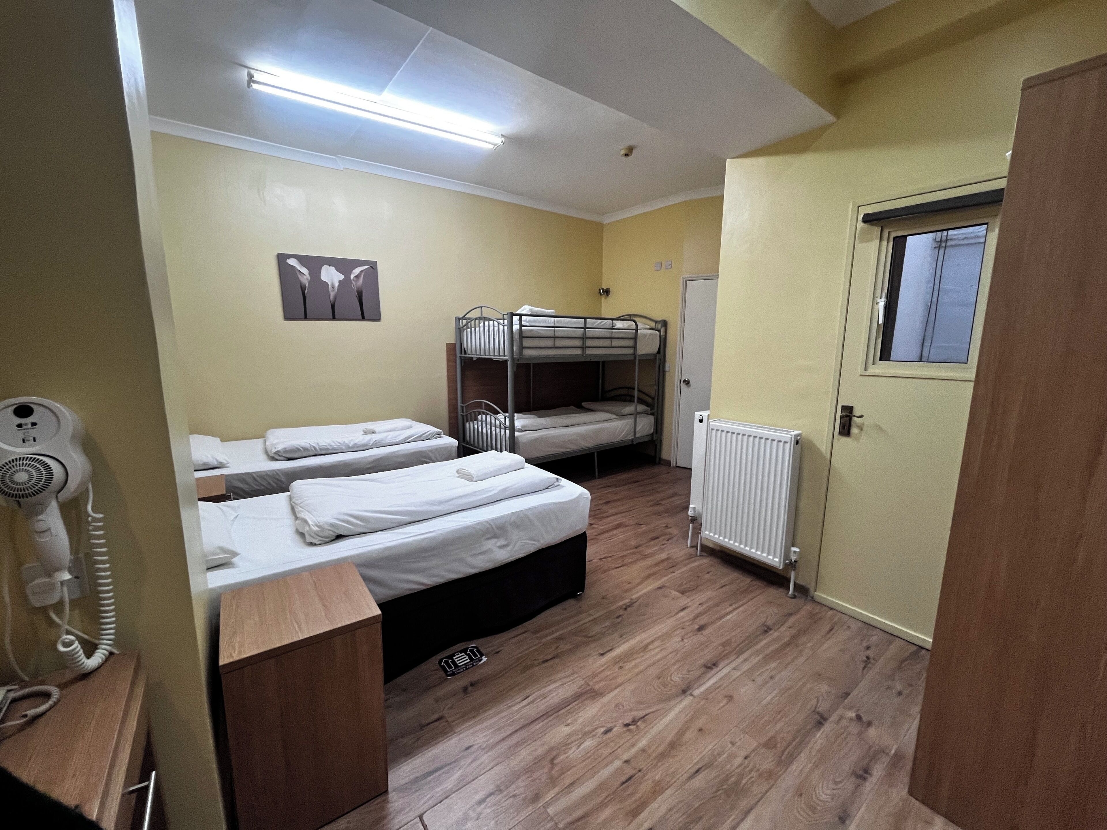 A dormitory room with bunk beds, a radiator, a wooden floor, and a ceiling light fixture.