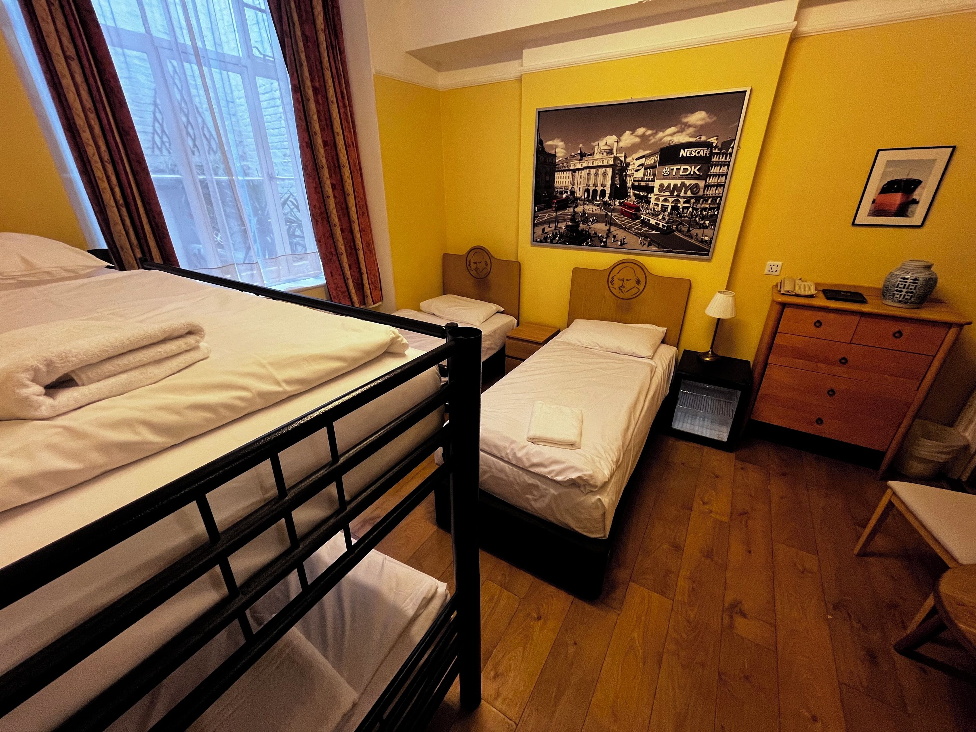 A hotel room with two beds, a wooden dresser, a nightstand, and a poster on the wall.