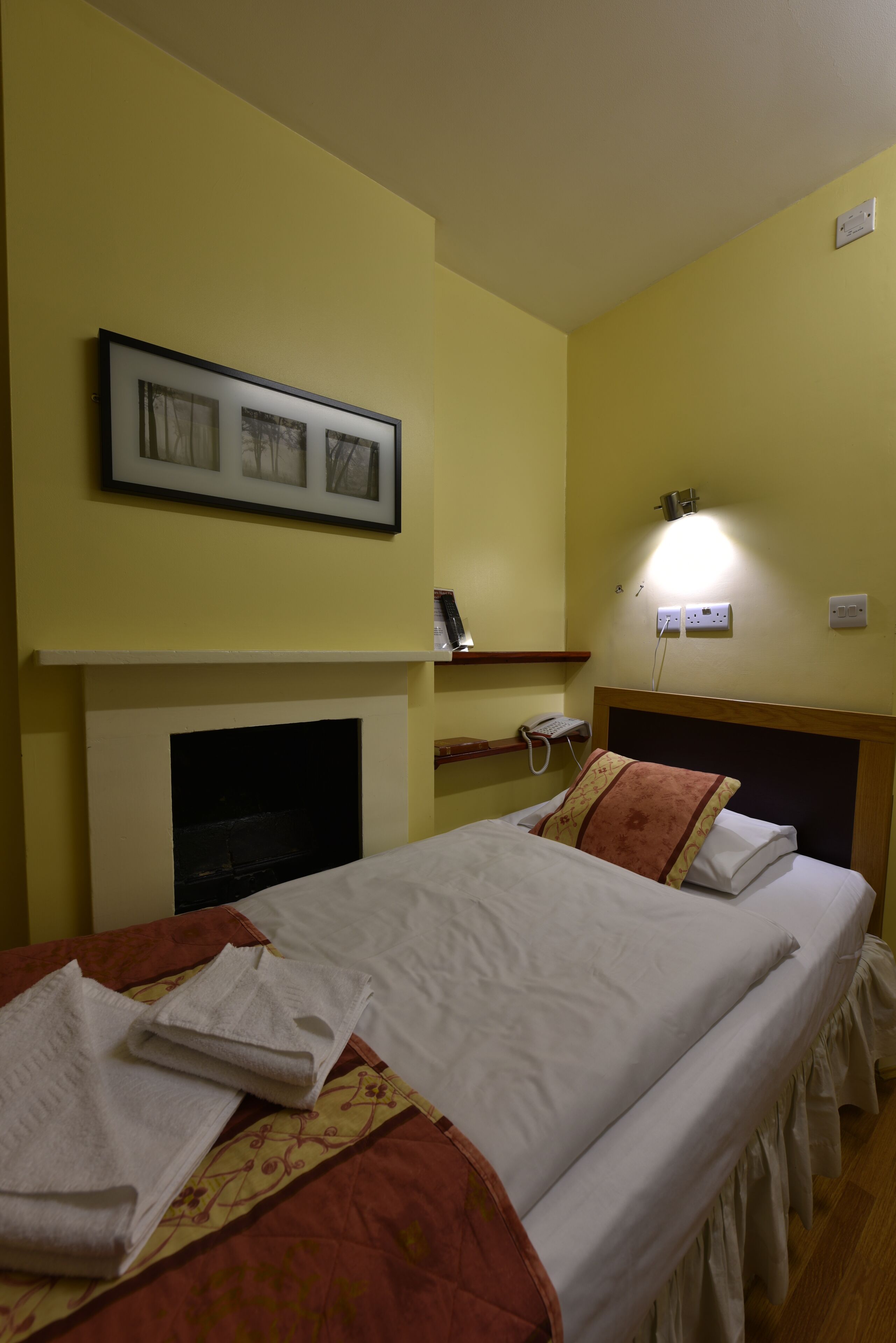 A hotel room with two beds, a fireplace, a wall-mounted shelf, and a bedside telephone.