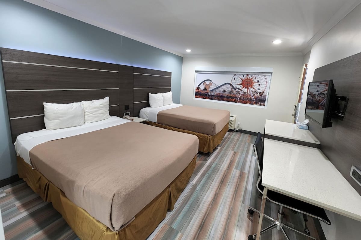 Habitación de hotel con dos camas, un escritorio, una televisión y un ventanal con un mural.