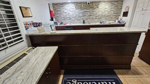 Hotellin vastaanottotiski marmoritasolla, «Travelodge»-kyltti, kehystetty laatta ja «Travelodge»-merkkinen eteisessä oleva matto.