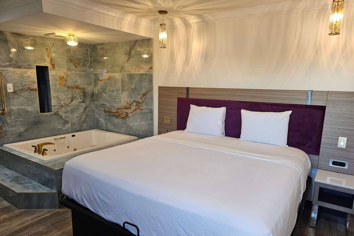 Una habitación de hotel moderna con una cama grande, una bañera independiente, paredes de mármol e iluminación contemporánea.