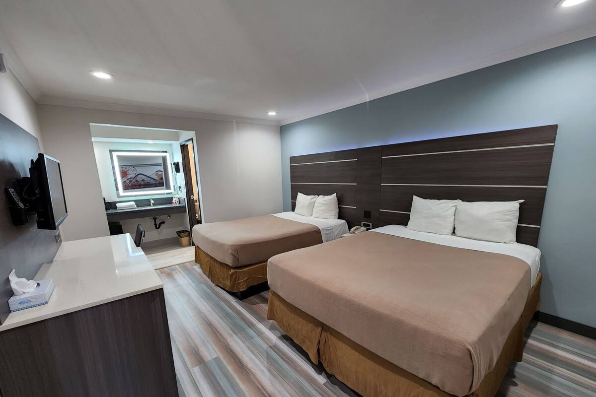 Una habitación de hotel con dos camas, un escritorio, un espejo y un televisor.