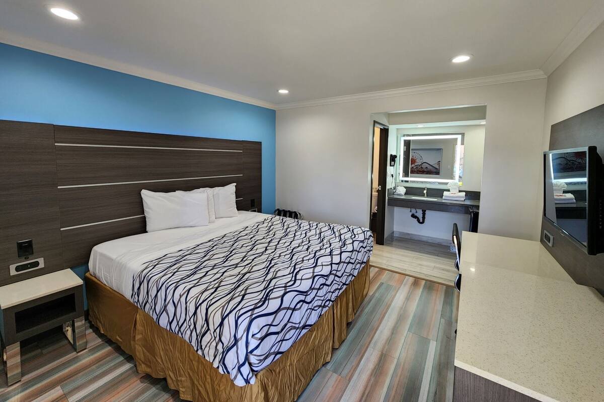Habitación de hotel con cama, mesita de noche, televisión y baño con espejo y lavamanos.