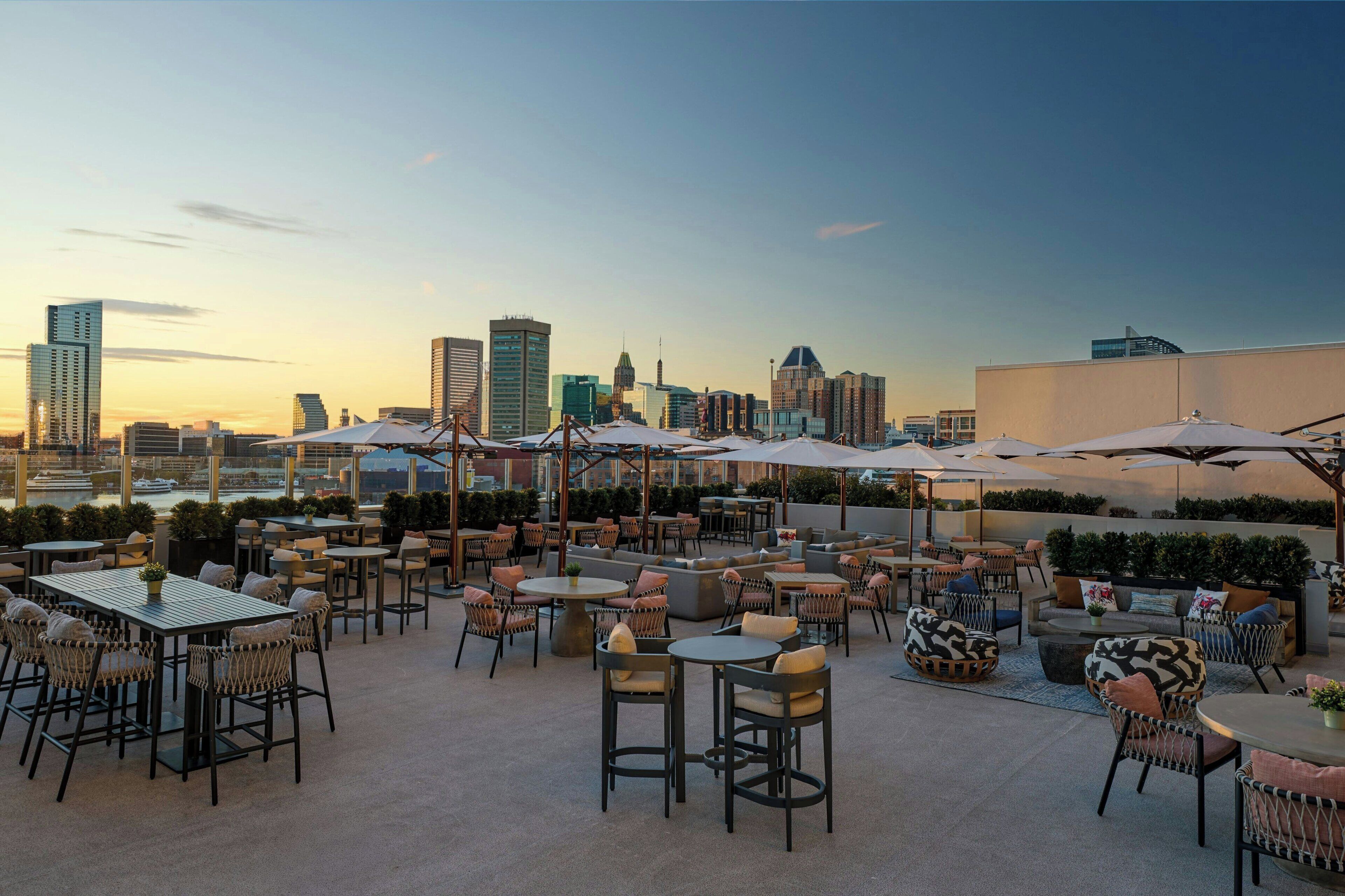 A rooftop patio with tables and chairs, umbrellas, and a city skyline view.