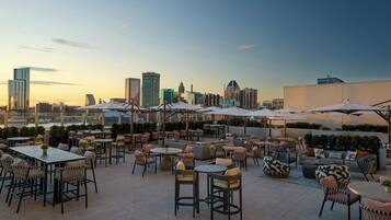 A rooftop patio with tables and chairs, umbrellas, and a city skyline view.